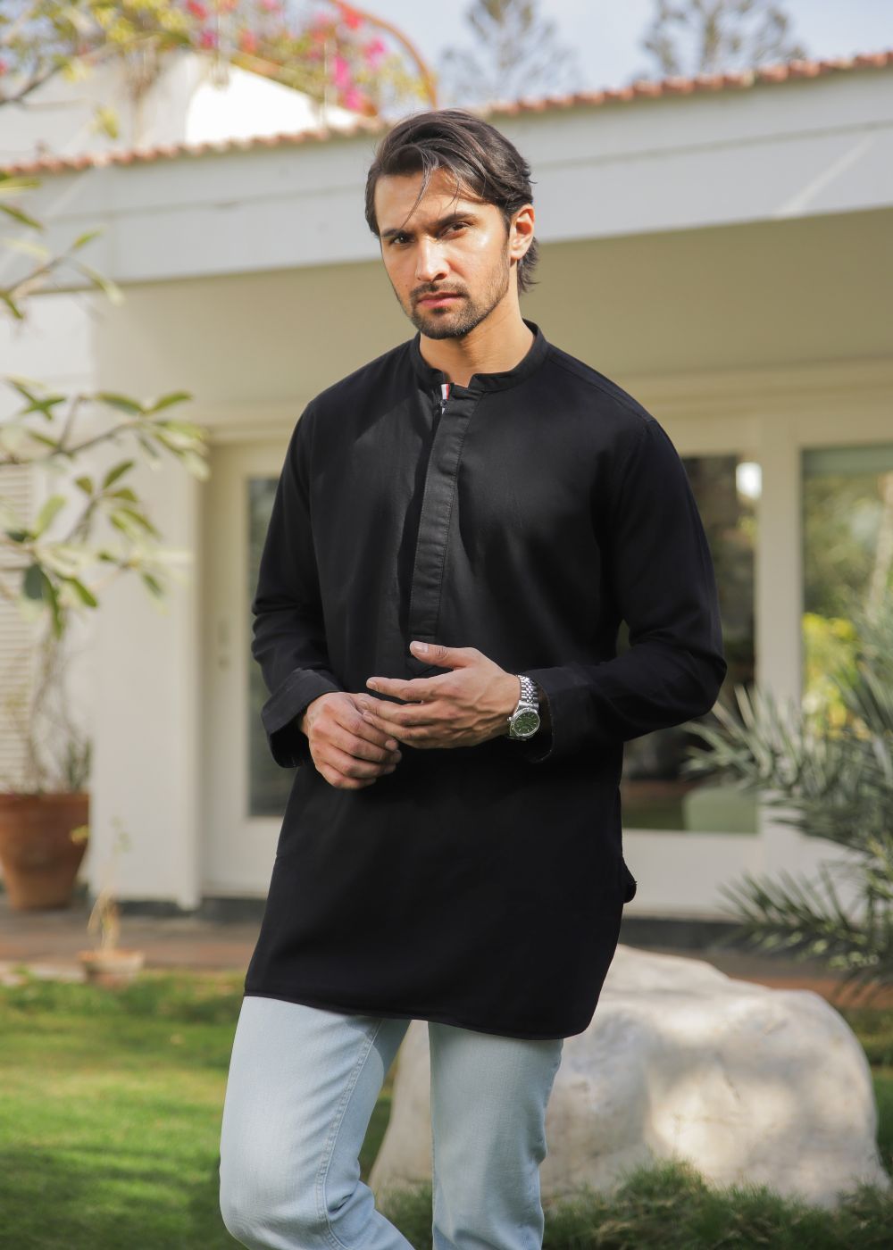 A man wearing a black kurta and light blue jeans standing in front of a house.